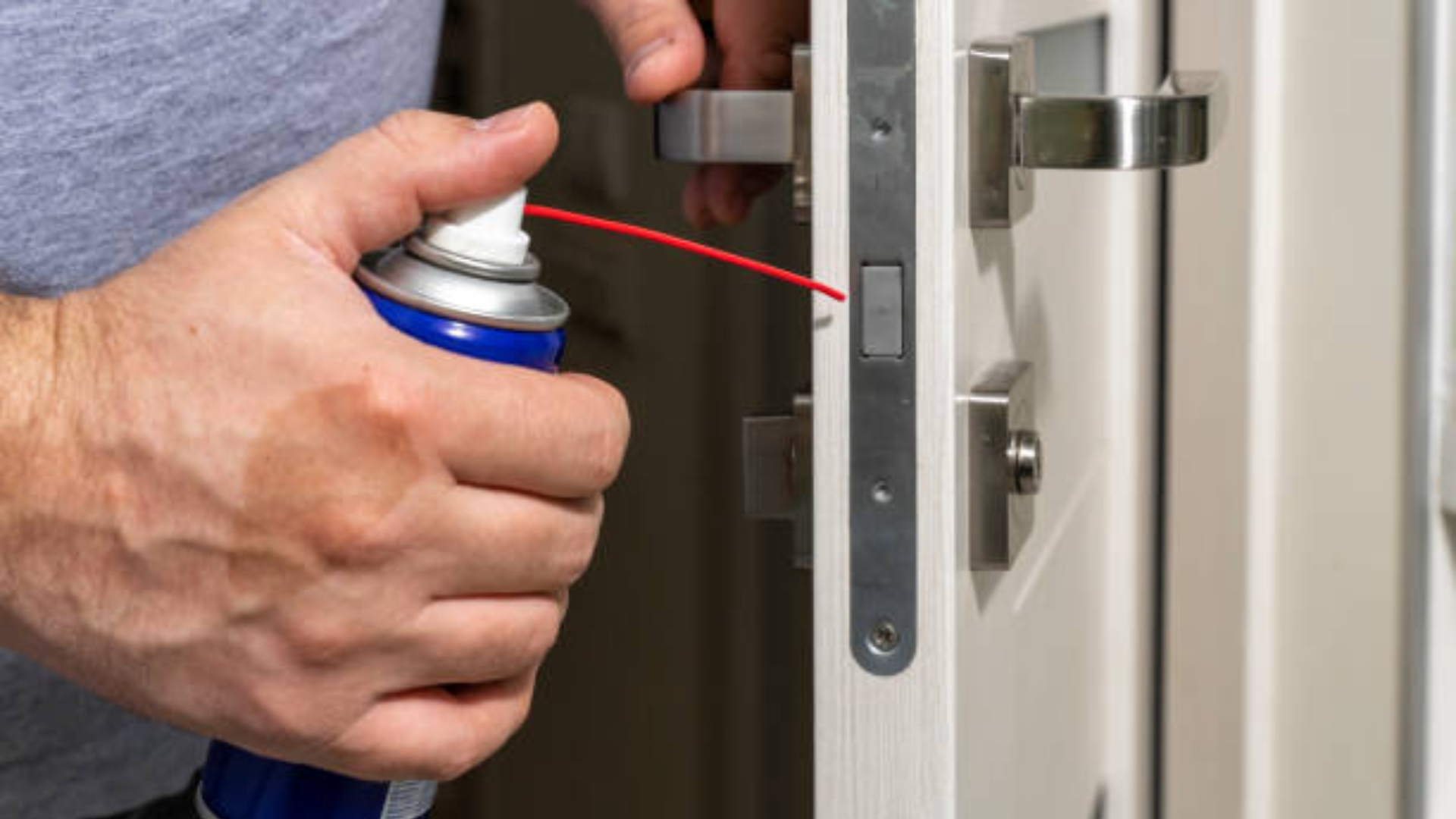A locksmith applying a dry door lock lubricant to a latch