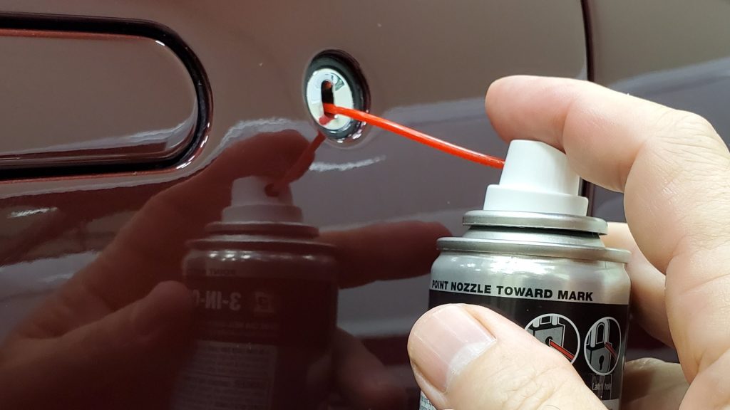 A person doing lock lubrication on a car
