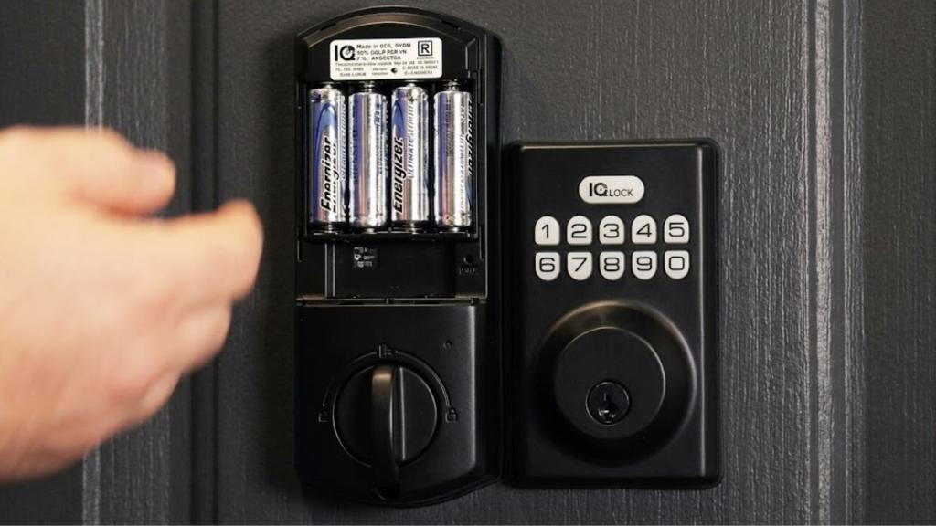 Close-up of a black keypad smart lock with its battery cover open, showing four AA batteries used to power the lock